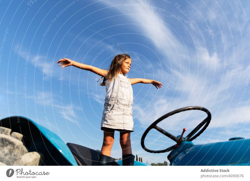 Carefree girl on tractor farm freedom outstretched arms agriculture sky clouds little kid child machinery vehicle equipment happy carefree countryside ranch