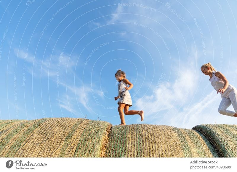 Siblings running on haystacks siblings farm sky clouds sunny daytime nature together boy girls lifestyle leisure family sisters brother teen kids children