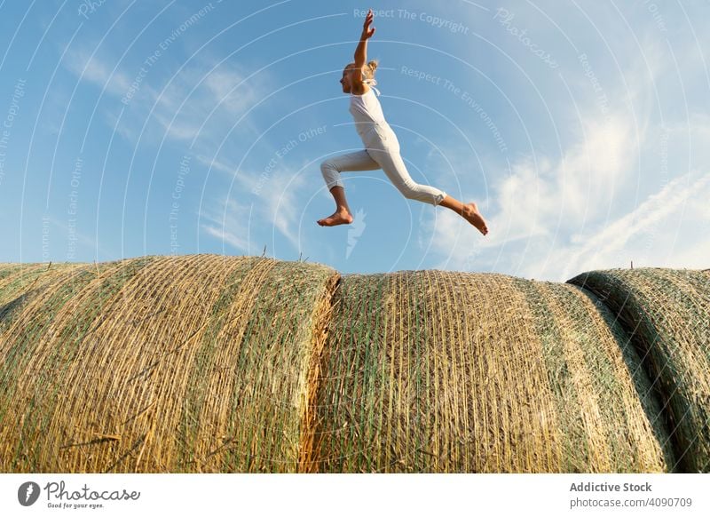 Barefoot girl running on haystacks farm sky clouds sunny daytime nature lifestyle leisure teen kid child barefoot dried grass straw rolls countryside rustic