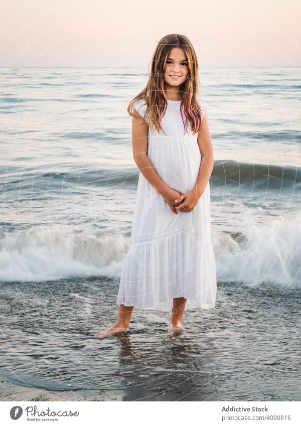 Smiling girl standing on seaside among waves portrait smiling charming water beach adorable summer beautiful female kid child childhood preschooler innocence