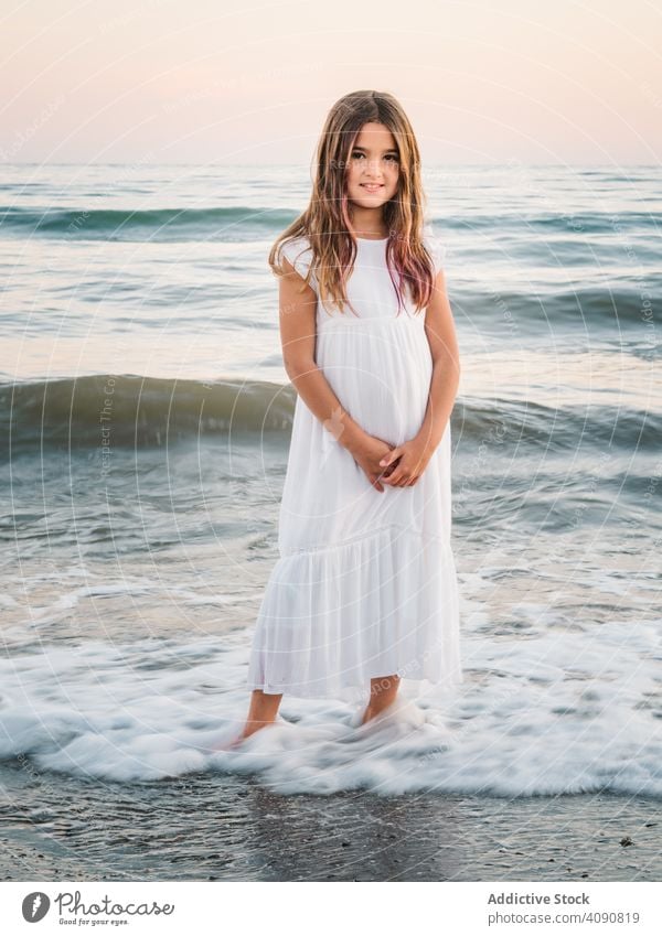 Smiling girl standing on seaside among waves portrait smiling charming water beach adorable summer beautiful female kid child childhood preschooler innocence