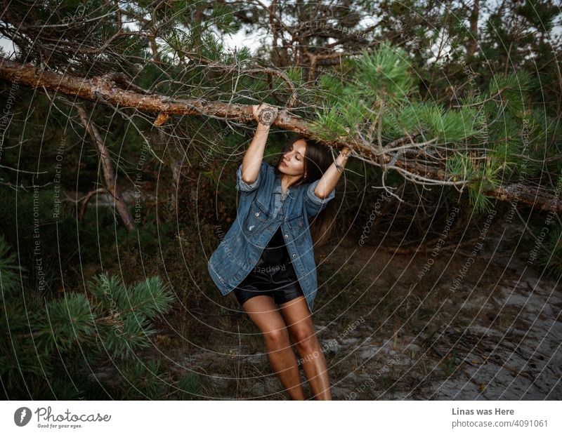 Wild and hot summer evening at dunes. Where the pines are green, and the girls are pretty. Like this beautifully tanned gorgeous brunette model. Dressed in blue jeans, with a tattoo on her hand, she enjoys the summertime.