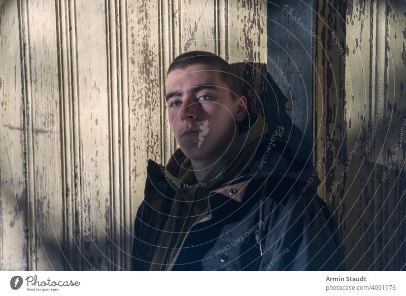 portrait of a serious young man leaning against an old wooden wall paint peeling grunge hoodie cool trendy shadow dark mysterious sunlight powerful confident