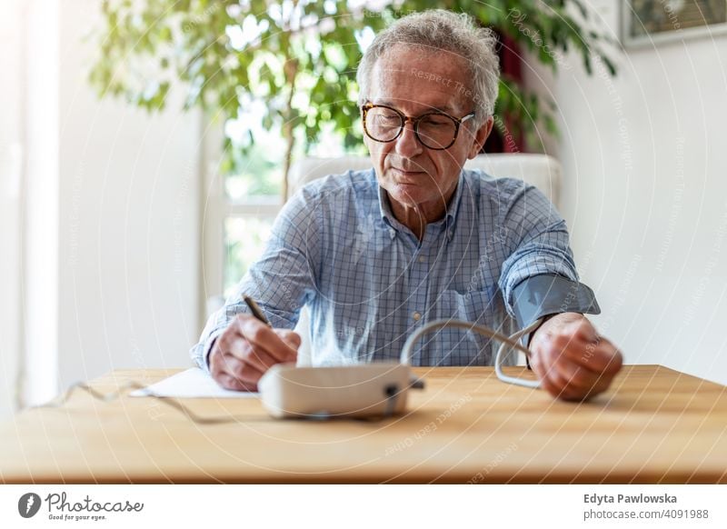 Senior man using medical device to measure blood pressure senior elderly grandfather old pensioner retired retirement aged mature home house male people