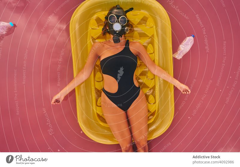 Female in gas mask and with plastic bottles in lake water woman environment sea respirator trash air mattress concept social pink swimsuit red lagoon recycle