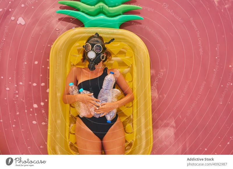 Female in gas mask and with plastic bottles in lake water woman environment sea respirator trash air mattress concept social pink swimsuit red lagoon recycle