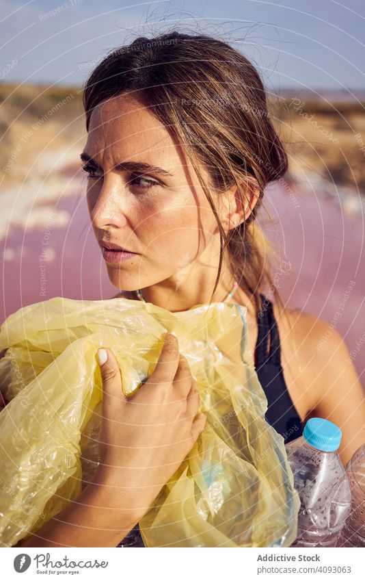 Concerned female in swimsuit collecting trash in natural lake pollution water contamination woman concerned pool pick bottle plastic red lagoon planet safety