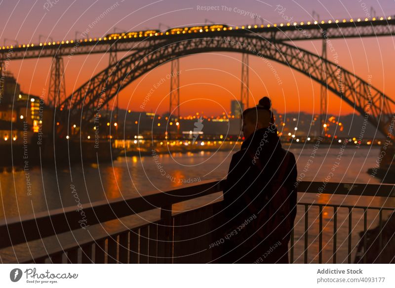 Female walking on embankment during sundown tourist city sunset bridge river border woman water architecture landmark sky cloudless female evening dusk twilight