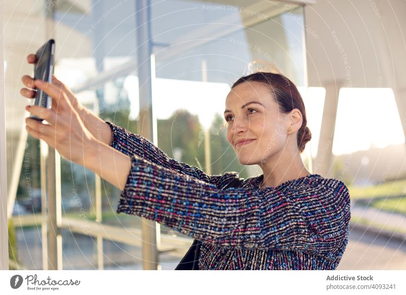 Smiling businesswoman taking selfie on street smartphone smile building office entrance modern city urban female cheerful work wall glass job mobile device