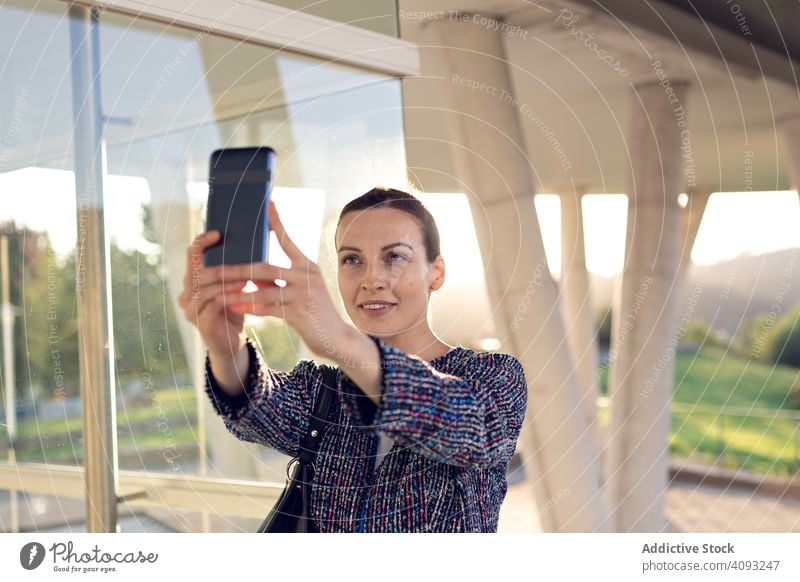 Smiling businesswoman taking selfie on street smartphone smile building office entrance modern city urban female cheerful work wall glass job mobile device