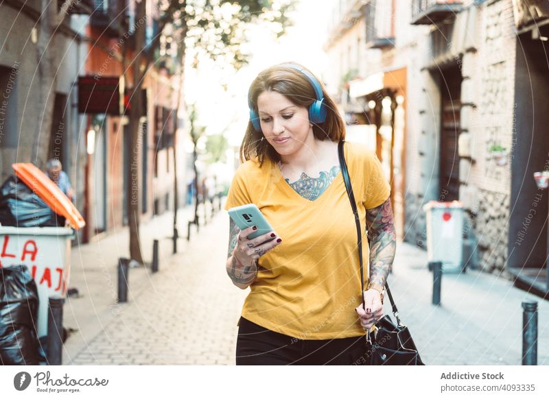 Inspired woman in headphones listening to music on smartphone on street hipster cool using streaming wireless attentive inspired tattooed stand sunny city town