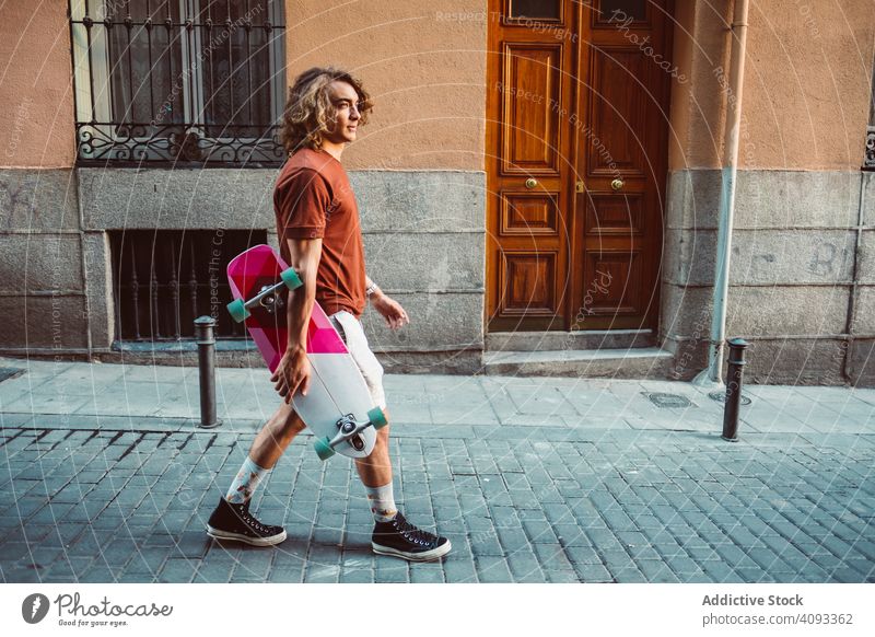 Man carrying longboard on the street man modern urban city stand hold sportive young adult fit strong extreme arm exercise lifestyle skater active fun skating