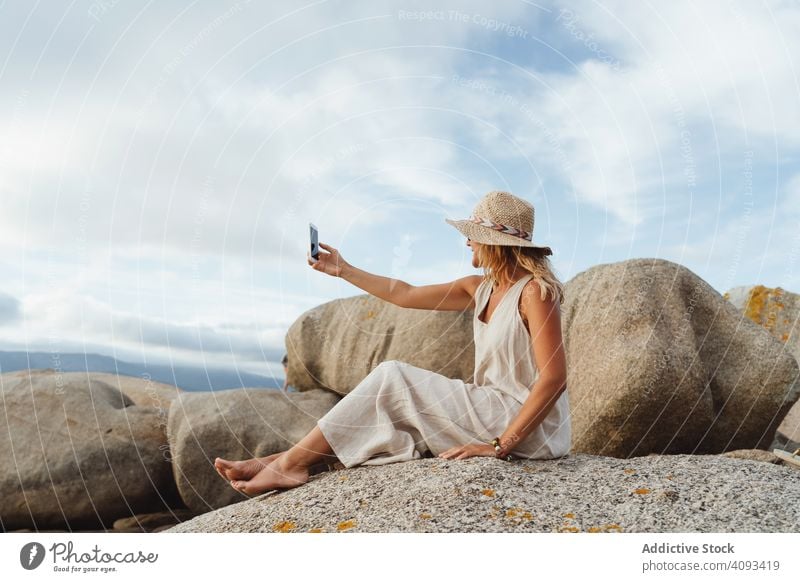 Contemporary woman with phone chilling on seashore smartphone coast alone enjoy escape travel seaside solitude remote wireless straw hat gadget trip vacation