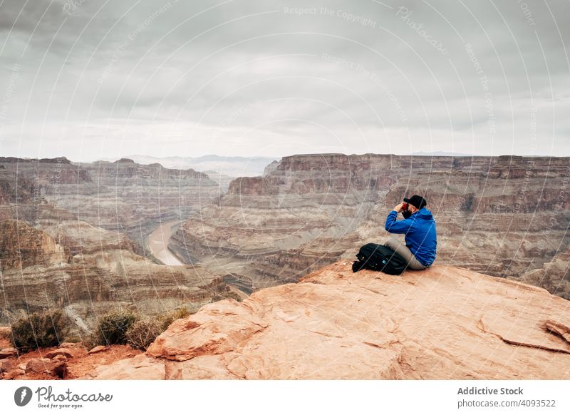 Male relaxing on cliff and admiring picturesque view canyon rest rock admire tranquil backpack jacket usa nature lifestyle hiking active sportswear sit mountain