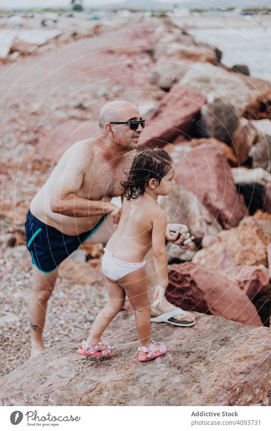 Grandfather and granddaughter having fun on rocky beach vacation grandfather ocean family elderly child girl water granddad nature shore enjoying retired