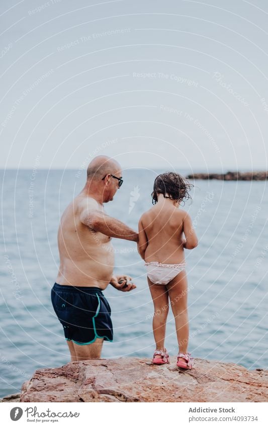 Grandfather and granddaughter having fun on rocky beach vacation grandfather ocean family elderly child girl water granddad nature shore enjoying retired