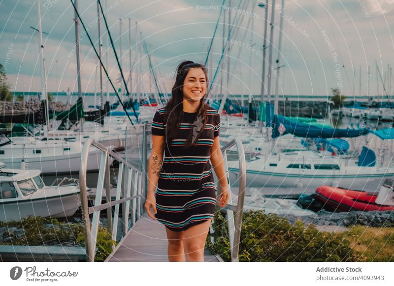 Smiling female walking along busy urban pier woman wharf harbor yacht enjoy boat sea nature happy summer young leisure seaside marina water transport vehicle