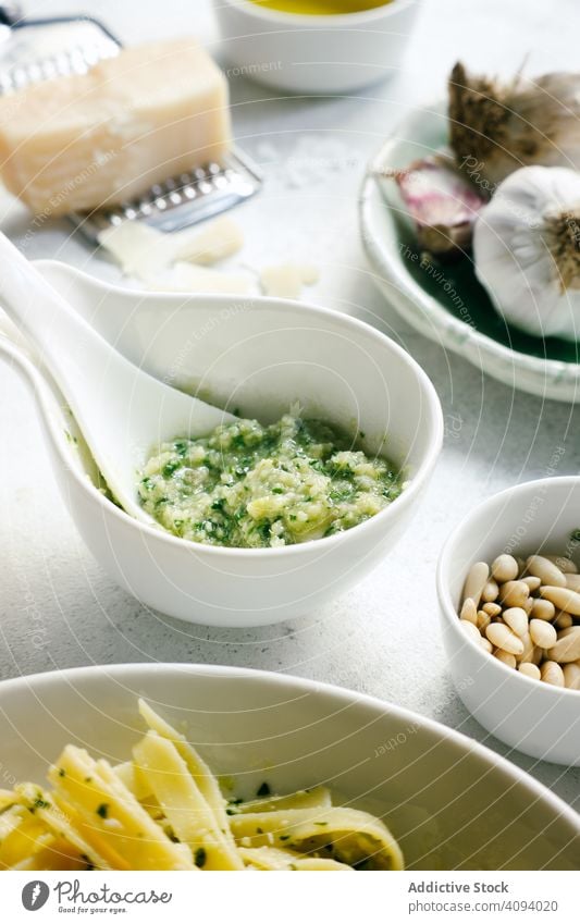 Bowl of fresh pesto sauce next to raw ingredients on table bowl garlic cheese pine nuts rustic white pasta food vegetarian green italian herb cuisine