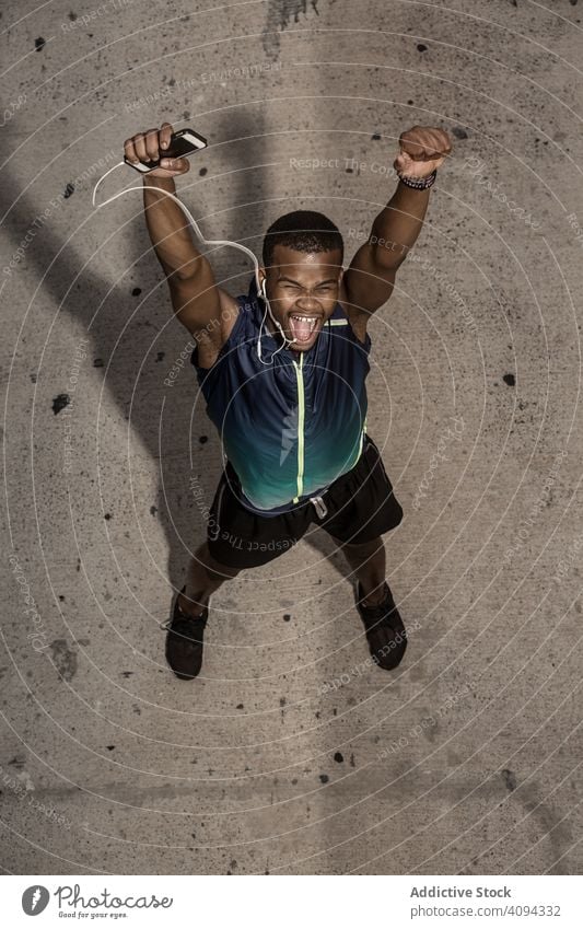 Excited ethnic sportsman in headphones celebrating success celebrate result race victory happy urban progress win excited competition muscle finish physique