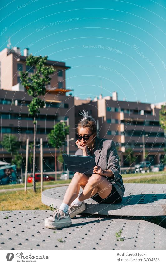 Stylish woman sitting and browsing tablet outside businesswoman street city urban lady internet using digital communication architecture fashion stylish model