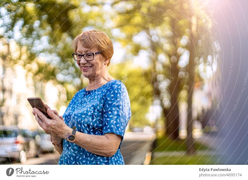 Portrait of a senior woman using mobile phone outdoors people mature casual female Caucasian elderly old grandmother pensioner grandparent retired retirement