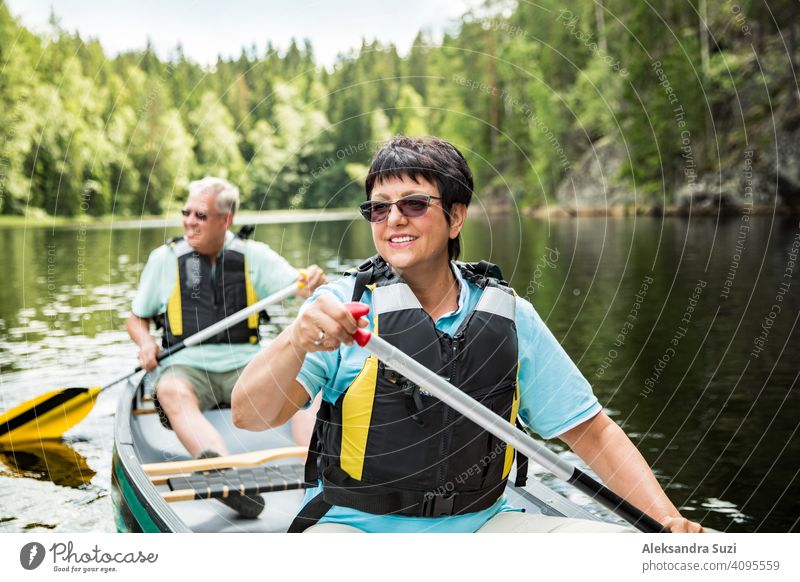 Happy mature couple in life vests canoeing in forest lake. Sunny summer day. Tourists traveling in Finland, having adventure. active activity beautiful discover