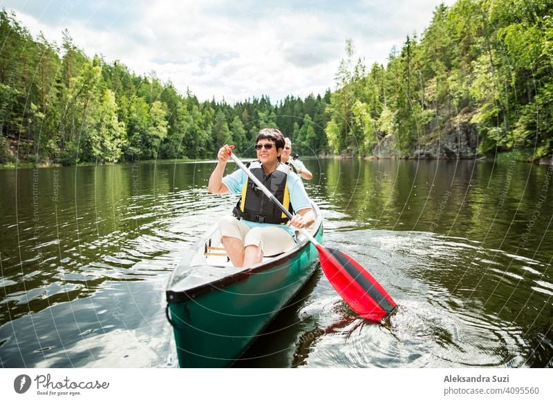 Happy mature couple in life vests canoeing in forest lake. Sunny summer day. Tourists traveling in Finland, having adventure. active activity beautiful discover