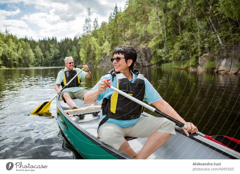 Happy mature couple in life vests canoeing in forest lake. Sunny summer day. Tourists traveling in Finland, having adventure. active activity beautiful discover