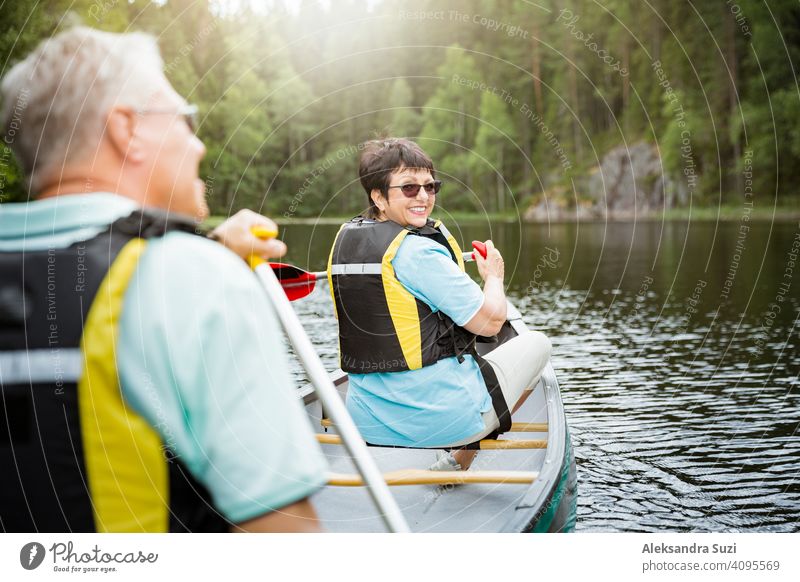 Happy mature couple in life vests canoeing in forest lake. Sunny summer day. Tourists traveling in Finland, having adventure. active activity beautiful discover