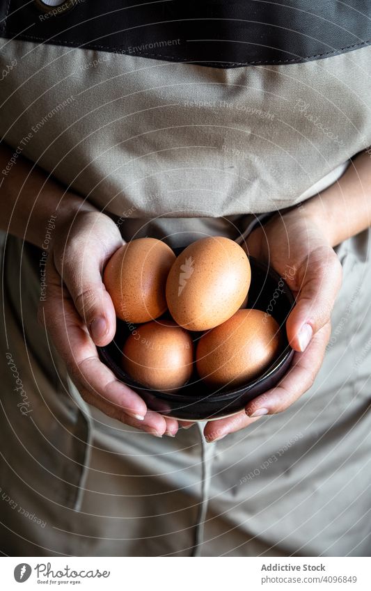 Faceless person holding bowl with eggs cook fresh cooking organic chicken handful ingredient food preparation healthy delicious adult shell apron gray brown