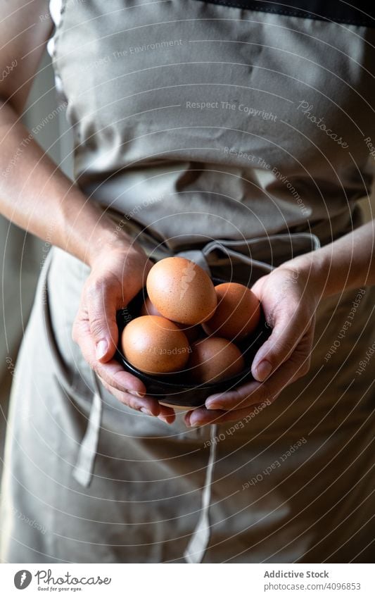 Faceless person holding bowl with eggs cook fresh cooking organic chicken handful ingredient food preparation healthy delicious adult shell apron gray brown