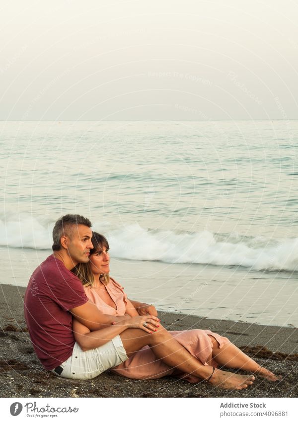 Delighted couple sitting on beach resort love hug date sea smile happy vacation man woman adult honeymoon summer shore coast relationship water embrace ocean