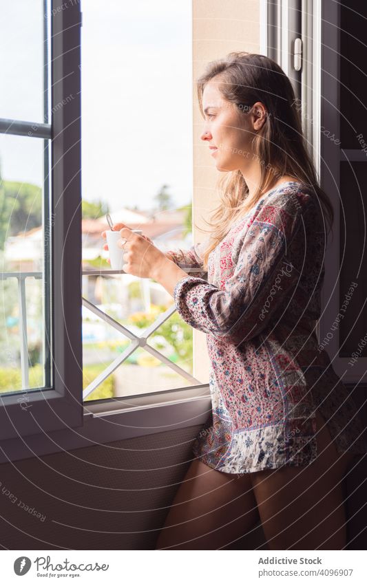 Girl in a shirt with a cup of coffee or tea looking out the window in the morning woman pretty awake joy girl beauty indoors view home rest lifestyle beautiful