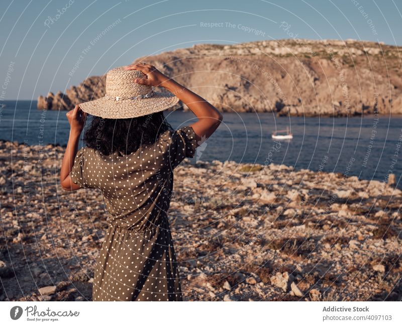 Romantic woman holding hat and looking at boat in sea seaside yacht vacation trip vessel ship summer adventure ocean beautiful female holiday fashion brunette