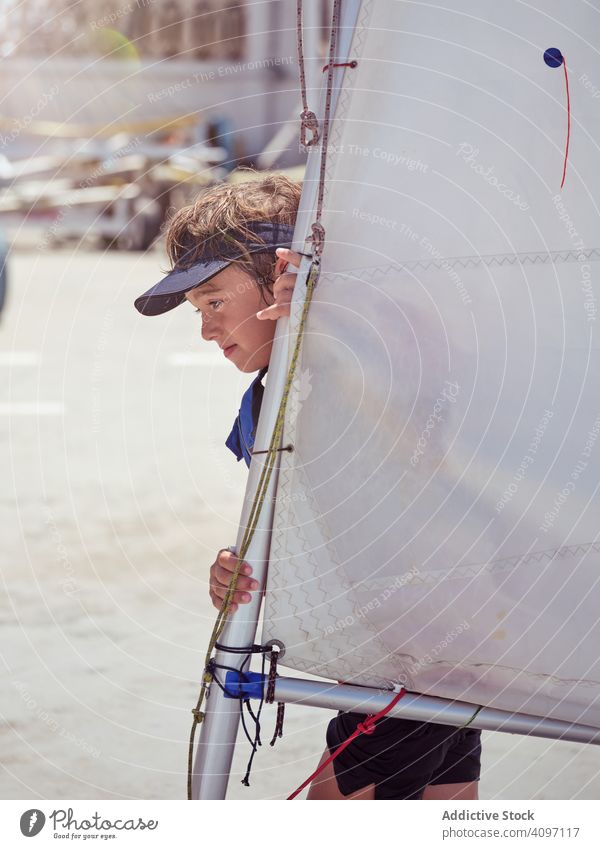 Skilled boy in blue life jacket carrying white sail walking yacht kid cruising water shore sport wind ocean holiday tense swimming childhood hobby fun wet