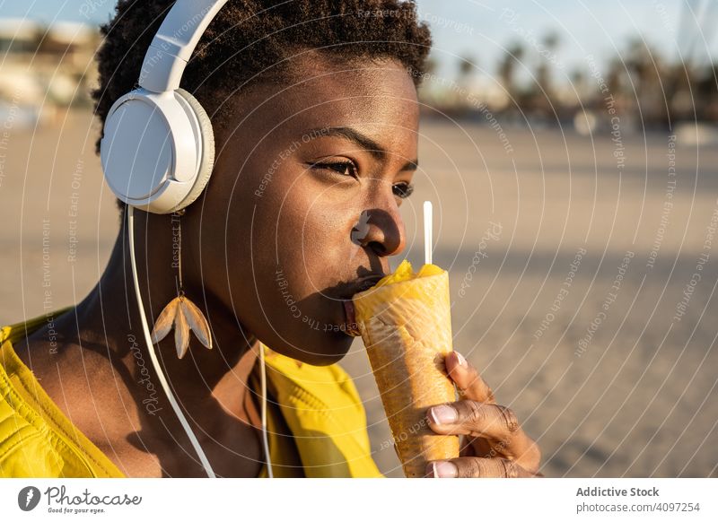 Cool female eating ice cream on beach woman trendy cool desert african american jacket yellow bright sunglasses enjoy sweet food summer fun stick frozen popular