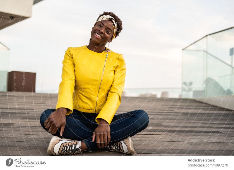 Smart woman sitting on wooden footpath stylish chill relax modern smart female floor jacket african american young cool trendy happy contemporary hangout cute