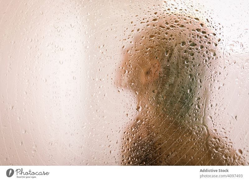 Woman behind wet glass in shower woman transparent partition bathroom water drop young female care body clean clear hygiene sensual translucent skincare routine