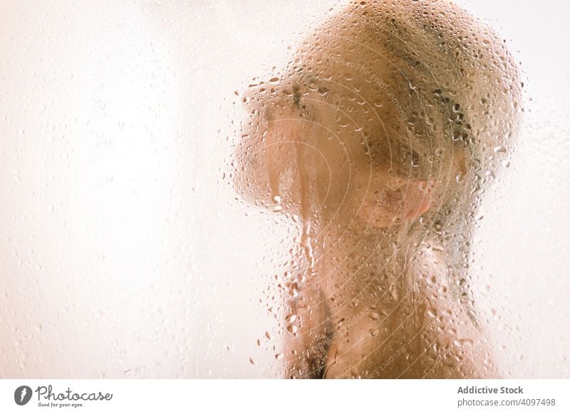 Woman behind wet glass in shower woman transparent partition bathroom water drop young female care body clean clear hygiene sensual translucent skincare routine