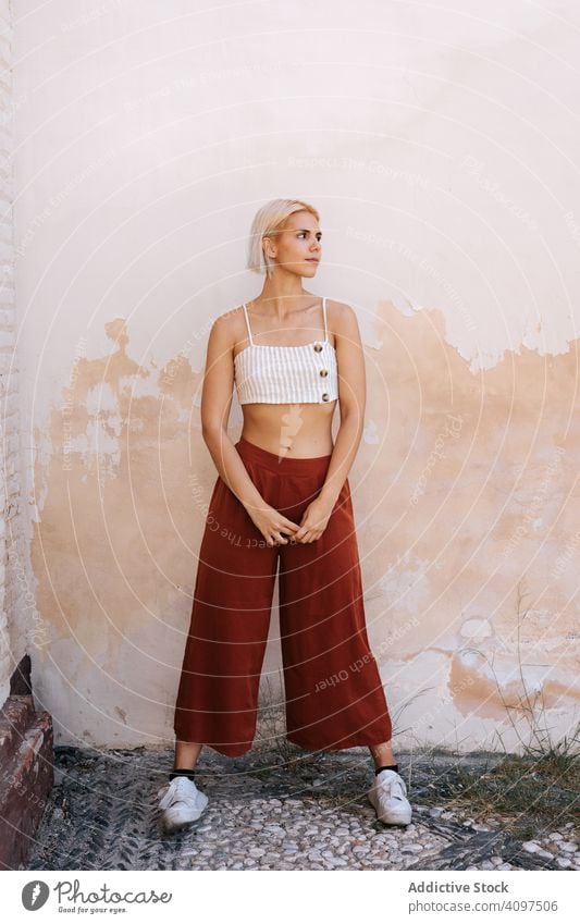 Young woman standing near crumbling wall shabby old stylish young slim city street female blond cheerful happy joy lean trendy casual weathered rough grungy