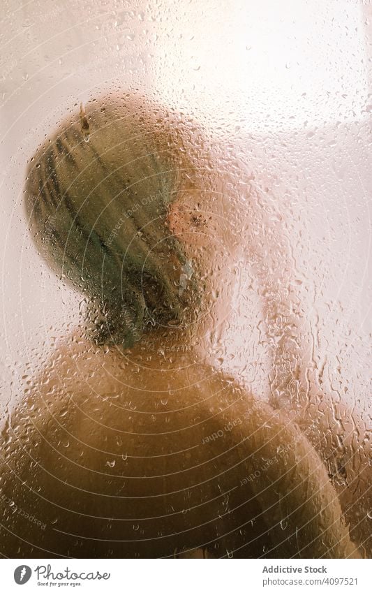 Woman behind wet glass in shower woman transparent partition bathroom water drop young female care body clean clear hygiene sensual translucent skincare routine