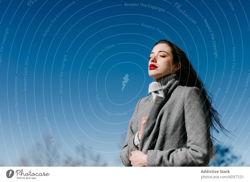 Young woman in coat on windy day stylish street closed eyes female fashion cool young model outfit warm weather exterior lady long hair trendy elegant vogue