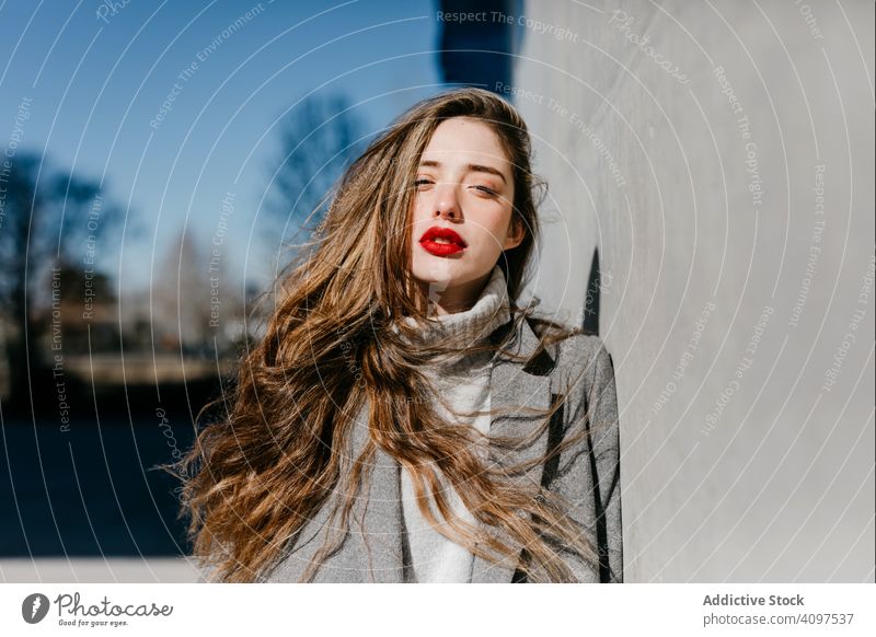 Young woman in coat on windy day stylish street wall city building female urban fashion cool young model outfit warm weather exterior lady long hair trendy