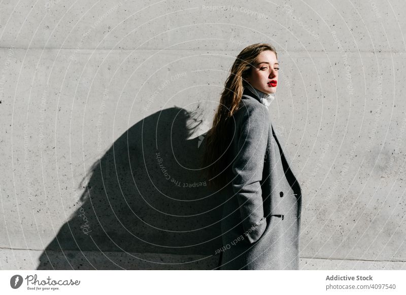 Young woman in coat on windy day stylish street looking at camera wall city building female urban fashion cool young model outfit warm weather exterior lady