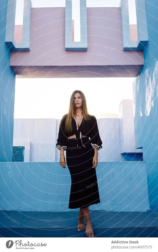 Woman standing on modern blue building woman long hair dress black elegant barefoot construction structure geometric architecture urban facade center wall