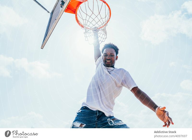 African American sportsman hanging on basketball lap kicking net slam dunk game player stadium playing sportswear activity field male powerful fit athlete