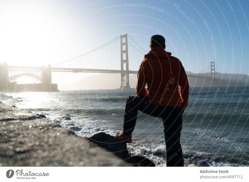 Tourist gazing at scenic bridge at peaceful bay tourist gaze sea coast man stand distant iron sun rays wave pier usa golden gate young adult mist landmark