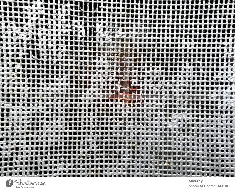 White wire mesh with thick white paint remains and red rust in the middle in Oerlinghausen near Bielefeld on the Hermannsweg in the Teutoburg Forest in East Westphalia-Lippe