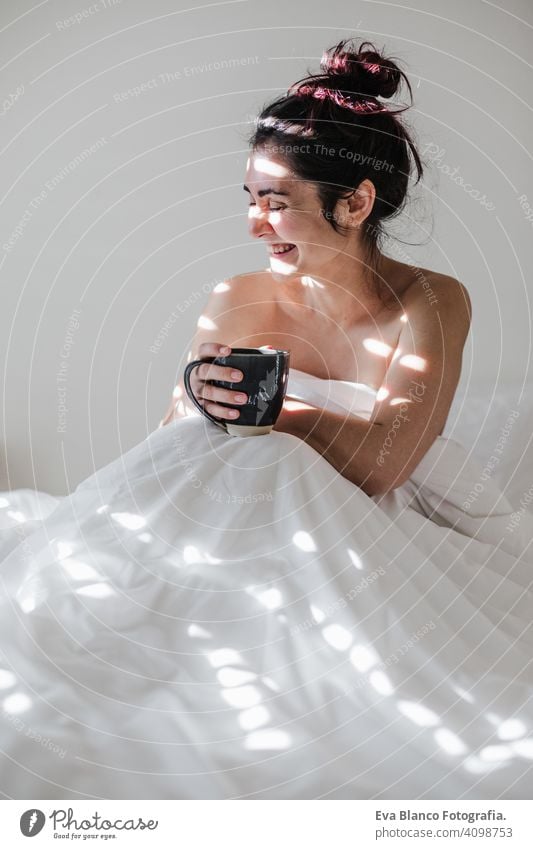 attractive young caucasian woman relaxing well in bed during morning time. Lady enjoys cup of coffee in bedroom breakfast drink beverage hot tea drinking