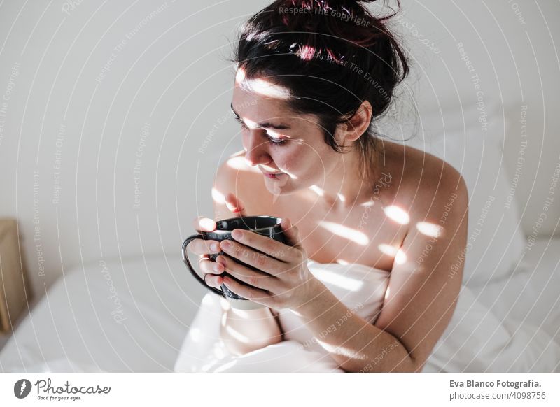 attractive young caucasian woman relaxing well in bed during morning time. Lady enjoys cup of coffee in bedroom breakfast drink beverage hot tea drinking